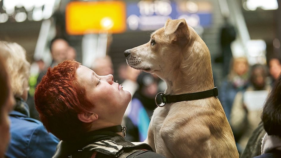 Frau hebt ihren kleinen Hund am Bahnhof hoch