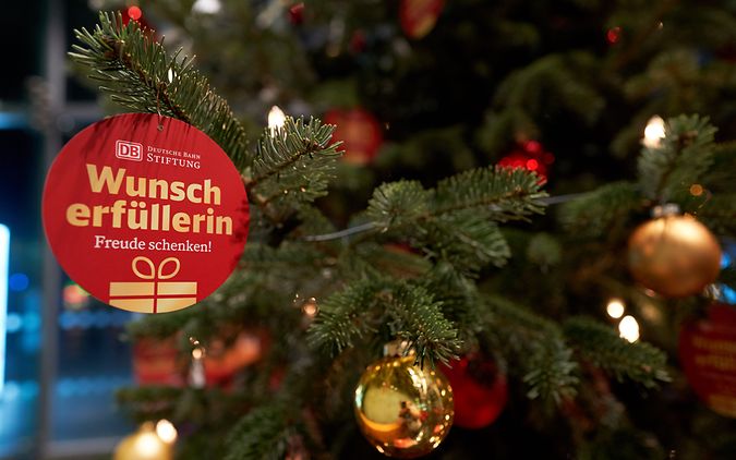 Weihnachtskugel mit "Wunscherfüller"-Schriftzug vor Weihnachtsbaum