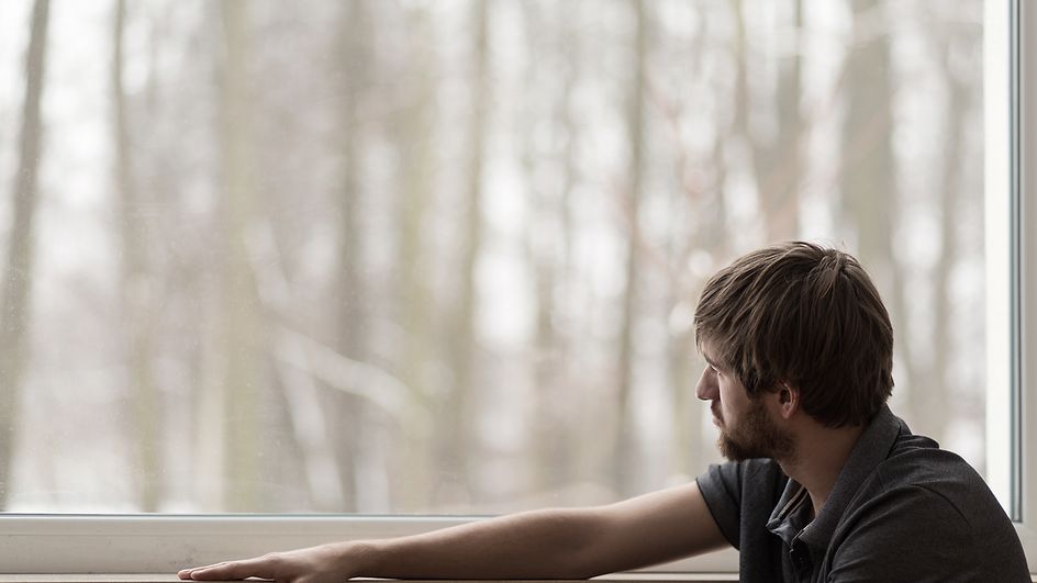 Mann schaut verzweifelt aus dem Fenster